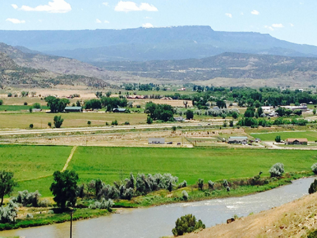 Colorado River flowing next to green pastures in the De Beque valley with Grand Mesa in the background